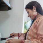 A South Asian woman in traditional clothing cooking indoors, showcasing cultural attire and cuisine.